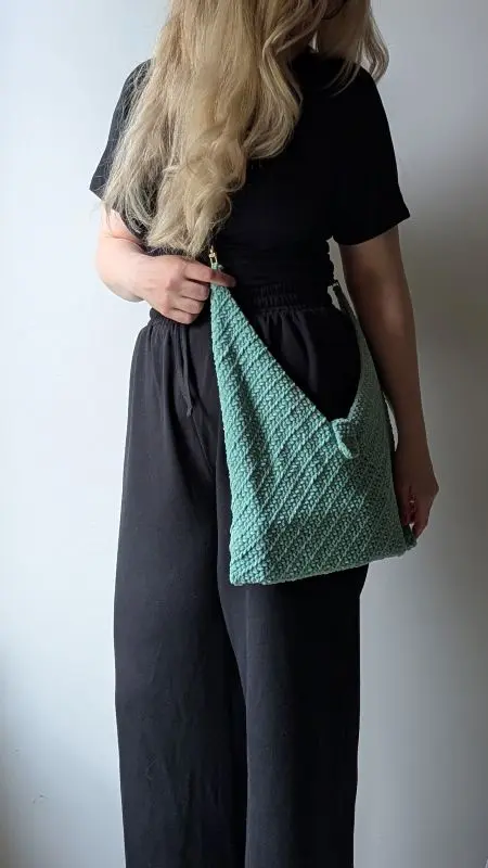Crochet Bag - Free Pattern - Make it in 1 weekend Woman holding a handmade mint-green crochet bag with textured stitches and a decorative clasp, styled with a black jumpsuit.