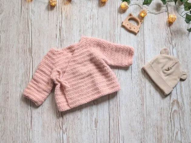 Baby crochet clothes pattern category cover featuring a soft pink handmade kimono sweater laid flat on wood background