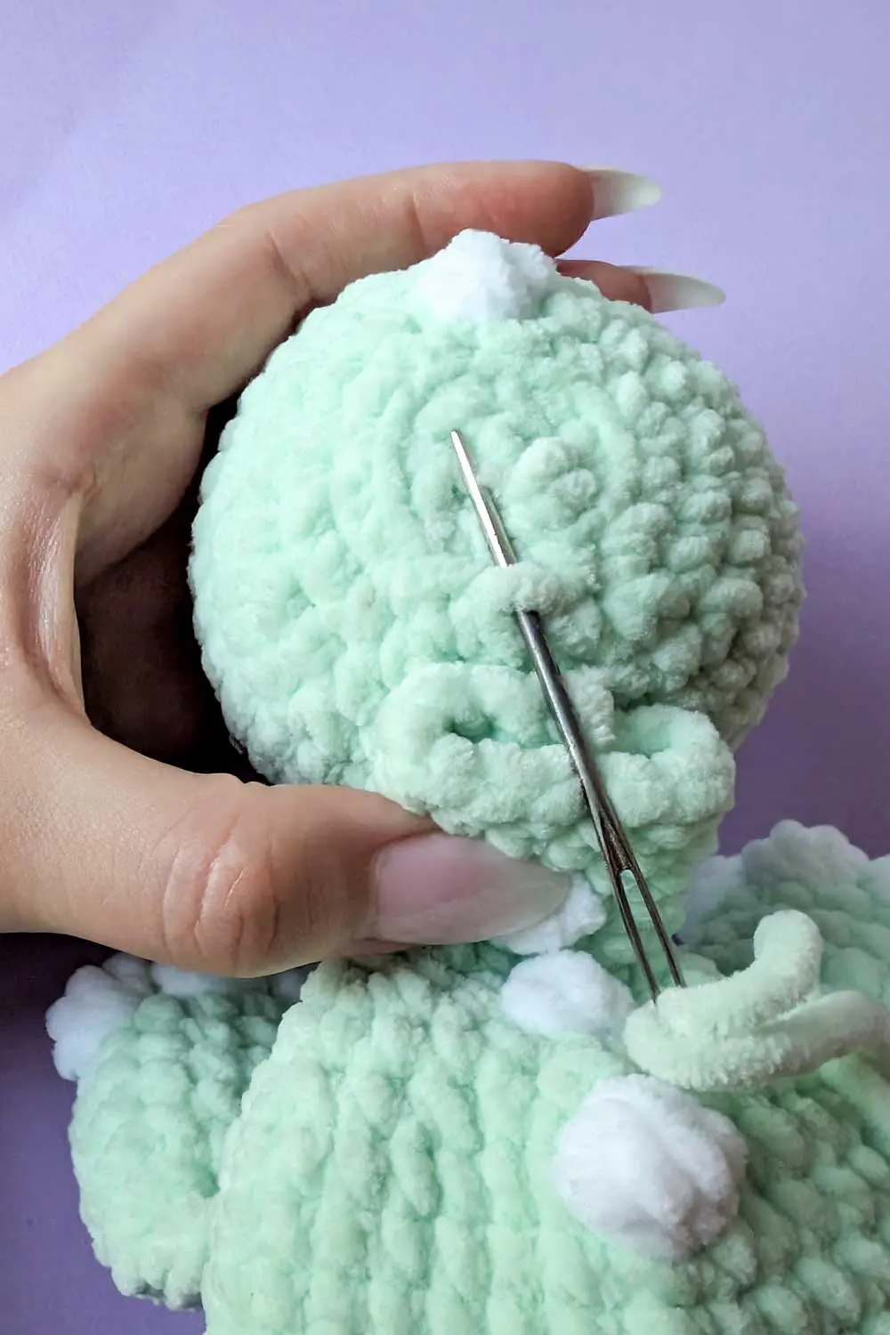 Crocheting a mint green dinosaur toy, displaying how to sew the head to the lovey body