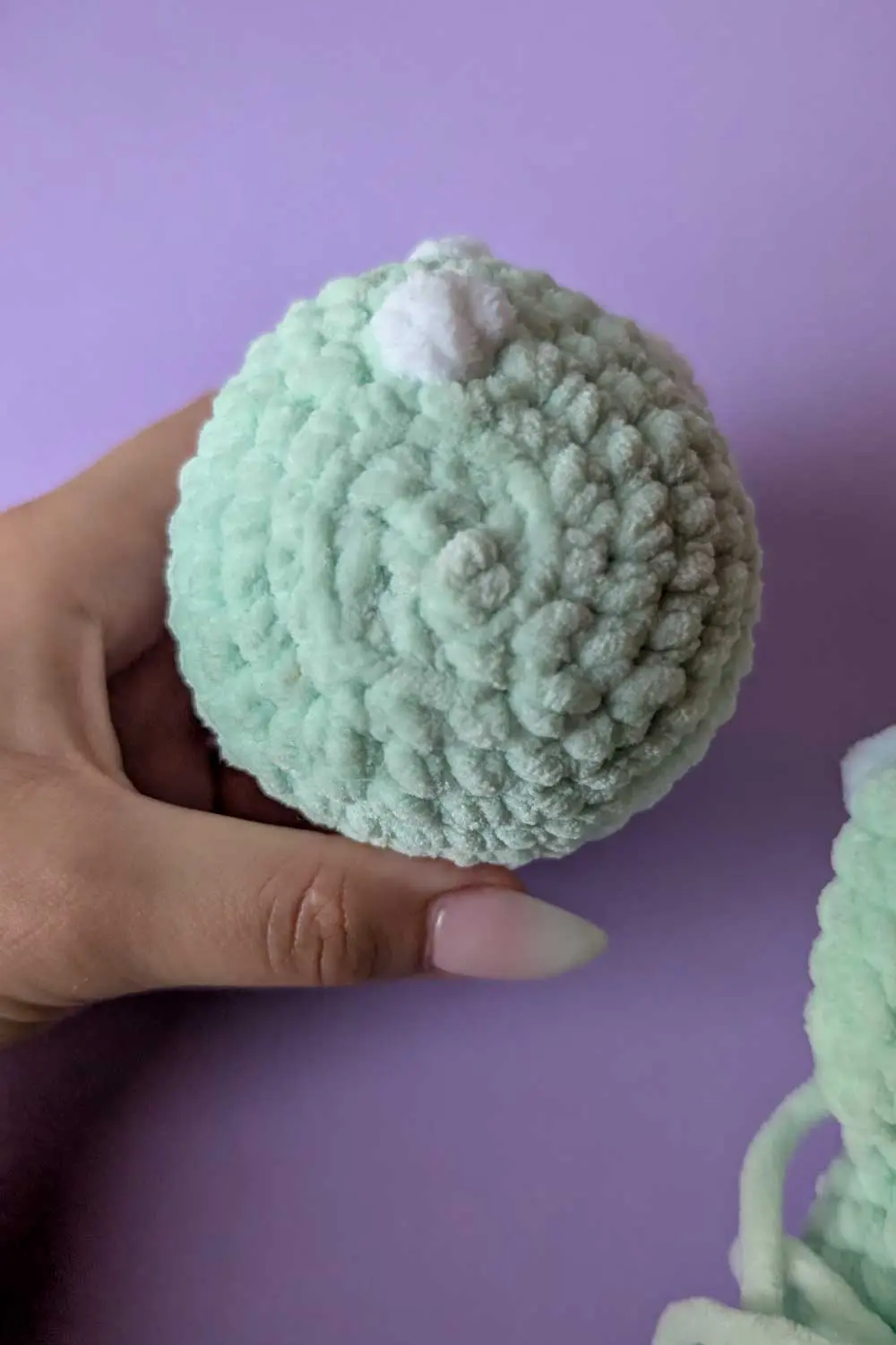 Hand holding a mint green crochet dinosaur head