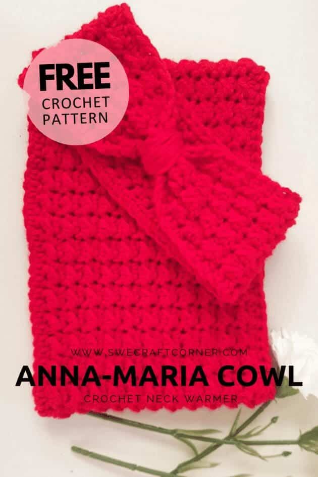 A bright red, crocheted cowl with a bow sits on a white surface next to a white flower. Text reads: Free crochet pattern. Anna-Maria Cowl. Crochet neck warmer. Find it at swecraftcorner.com.