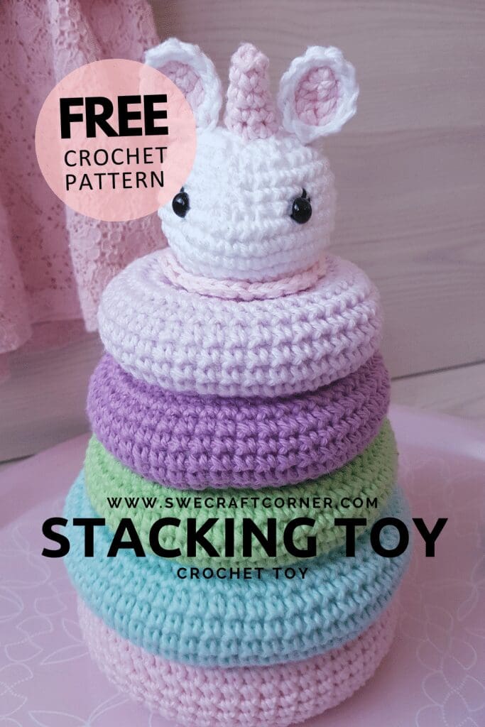 A crochet stacking toy shaped like a unicorn, featuring pastel rings in pink, purple, green, and blue. Text on the image highlights a free crochet pattern from swecraftcorner.com.