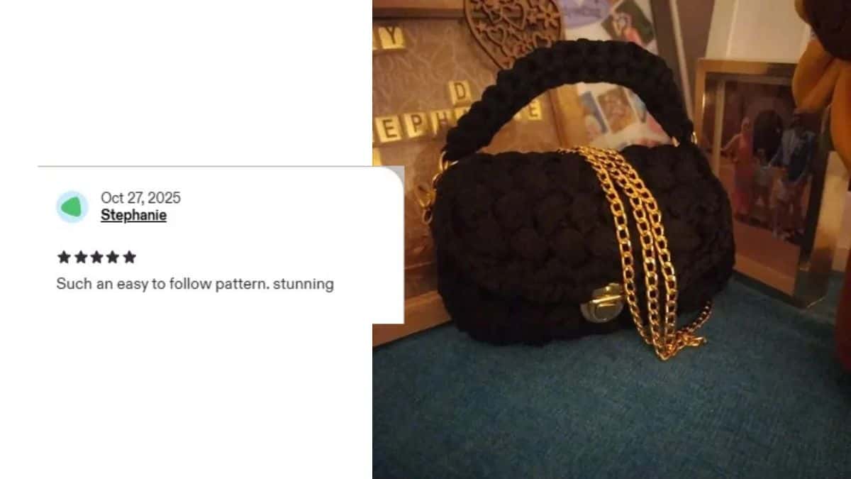 A black crocheted handbag, crafted from T-shirt yarn, with a gold chain rests on a blue surface. Nearby are framed decorations. A five-star review praises the easy crochet pattern and stunning result of this stylish clutch.
