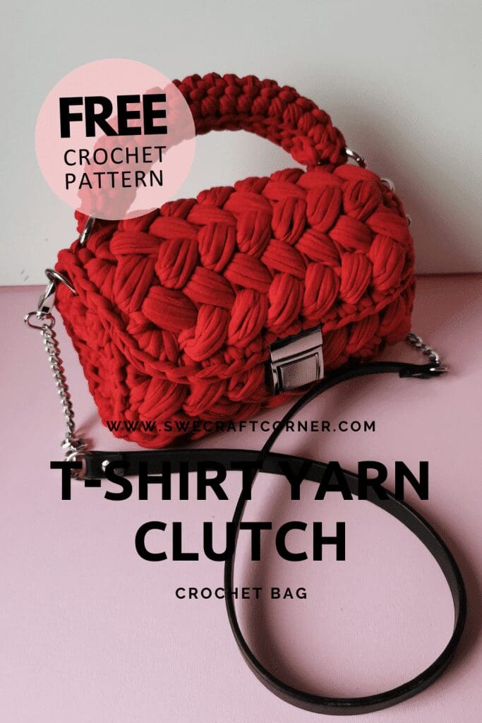 A red crocheted clutch bag with a chunky texture and silver hardware sits on a pink surface. Text reads: “FREE crochet handbag pattern. T-shirt yarn clutch crochet bag.” Black strap and website name are also visible.