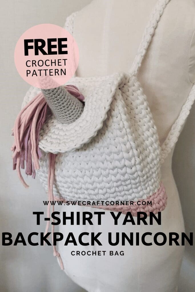 A white crochet unicorn backpack with a horn and pink, purple, and gray yarn mane, displayed on a mannequin. Text reads: FREE unicorn backpack crochet pattern - learn how to make a back pack with this fun T-shirt yarn project.