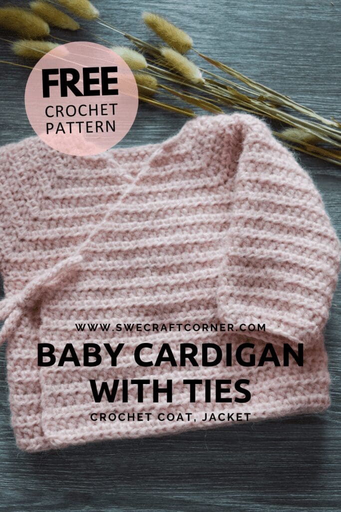 A soft, light pink crocheted baby cardigan with ties—perfect for fans of baby crochet clothes—is laid on a dark wood surface. Text on the image promotes a free crochet pattern for the cardigan from swecraftcorner.com. Dried grass is visible in the background.