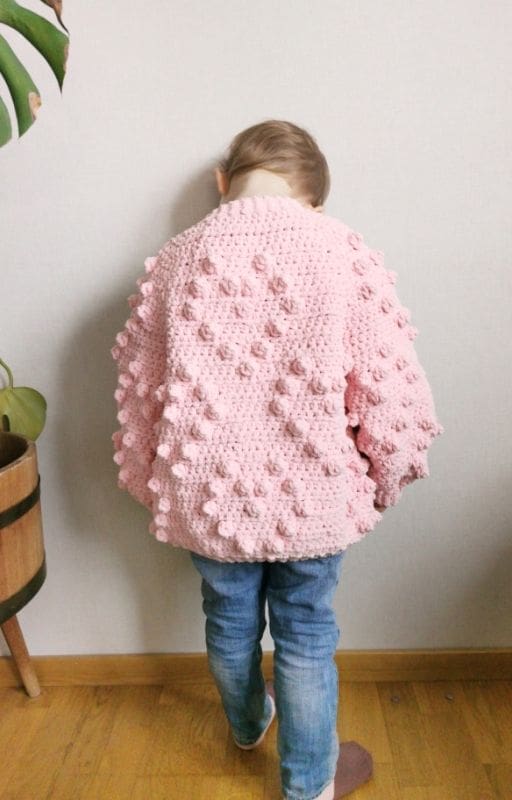 Crochet the Bobble Stitch Heart Cardigan for kids - Free pattern Toddler wearing a pink crochet heart cardigan with bobble stitch hearts on the back.