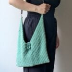 Mint crochet bag with unique texture and center clasp held by woman in black outfit.