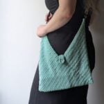 Mint crochet bag with unique texture and center clasp held by woman in black outfit.