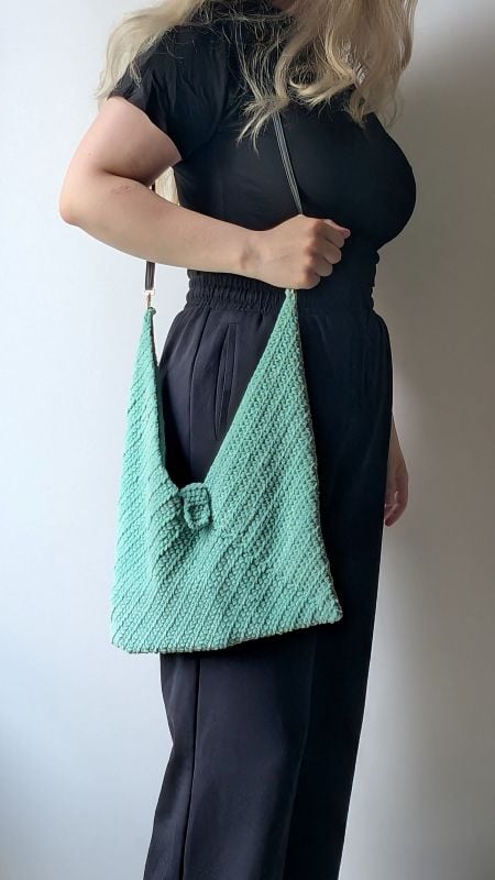 Woman holding a handmade mint-green crochet bag with textured stitches and a decorative clasp, styled with a black jumpsuit. The crochet bag is made using the free bag crochet pattern in the article