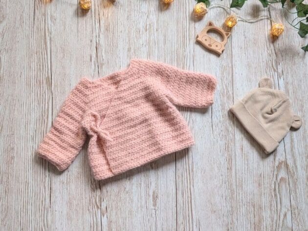 Baby crochet clothes pattern category cover featuring a soft pink handmade kimono sweater laid flat on wood background