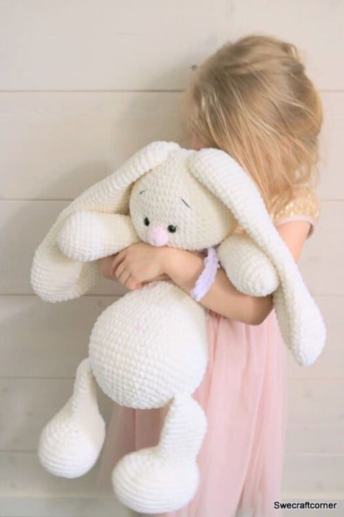giant crochet bunny pattern in white yarn held by a child in a pink dress against a light wood wall