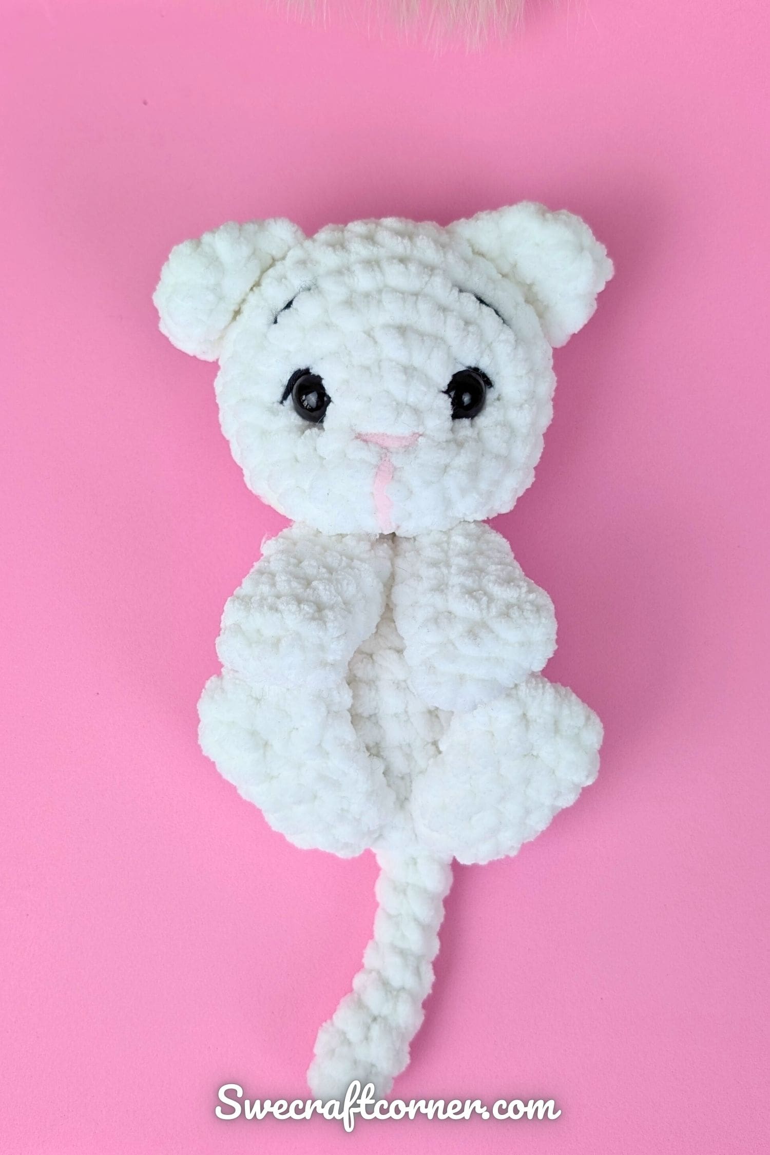 White crocheted cat plushie on pink