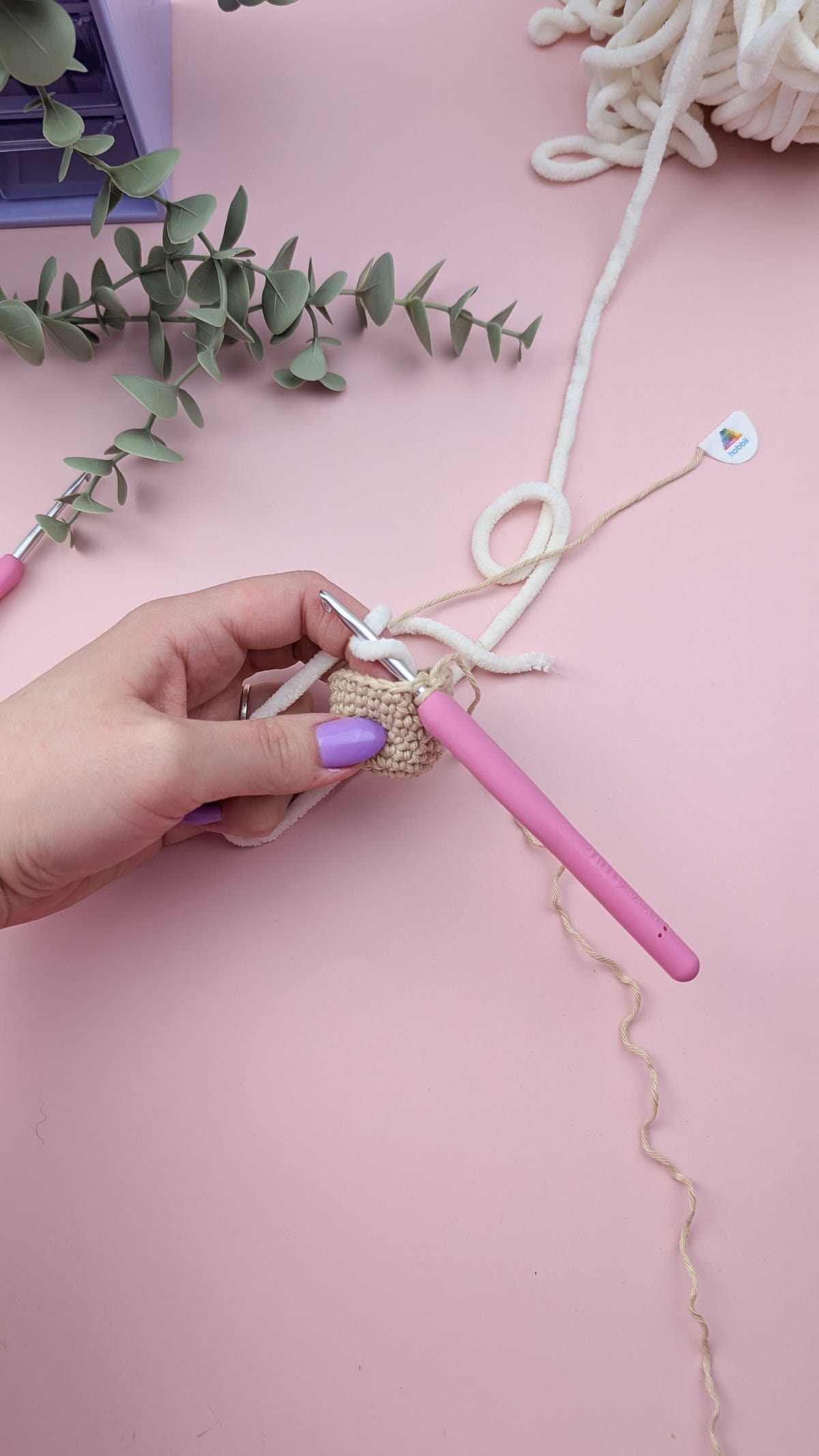 hands showing how to switch from the cotton to chenille yarn on pink background
