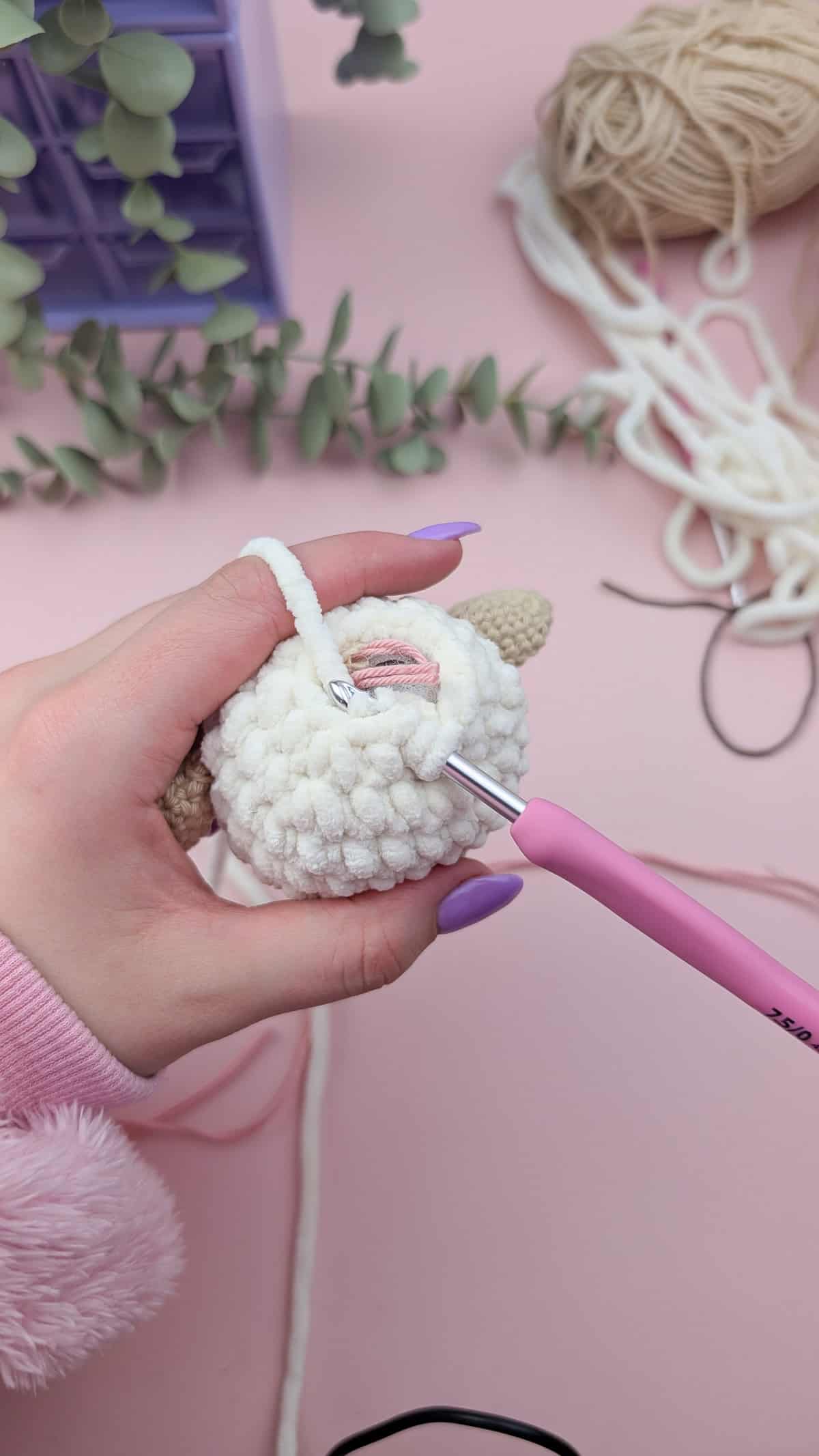 showing how to crochet the head closed with a pink crochet hook with white chenille yarn