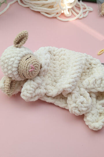 crocheted Lamb lovey laying on a pink background