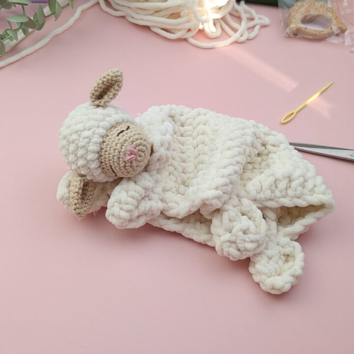 crocheted Lamb lovey laying on a pink background