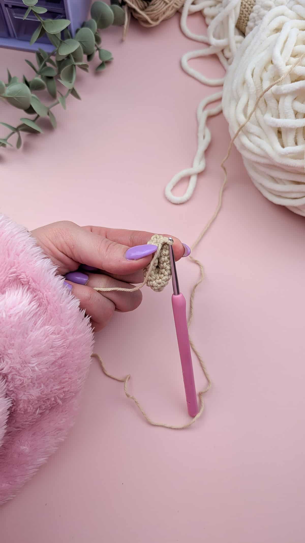 showing how to pinch the crocheted ear on a pink background